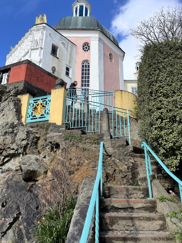 A view up winding steps with blue railings to a pink domed building.