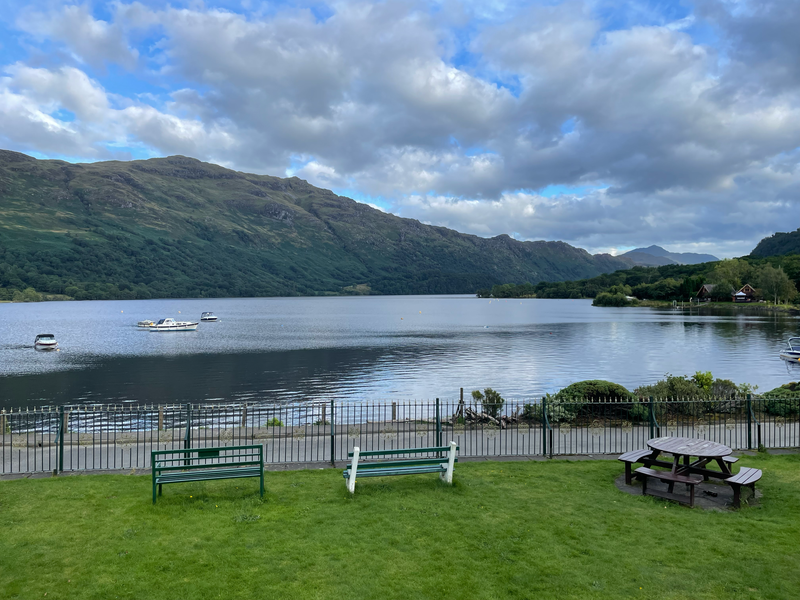 A view across a loch to mountains with boats and buoys in the foreground.