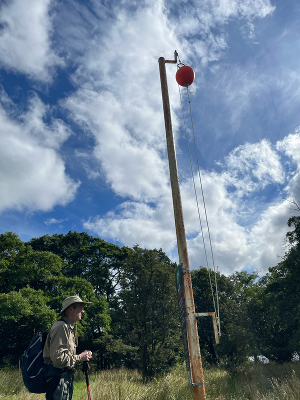 B. next to a tall post with an orange ball at the top.