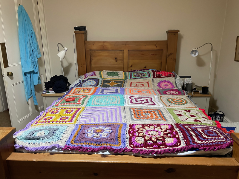 Blanket of miscellaneous crochet squares on a bed.