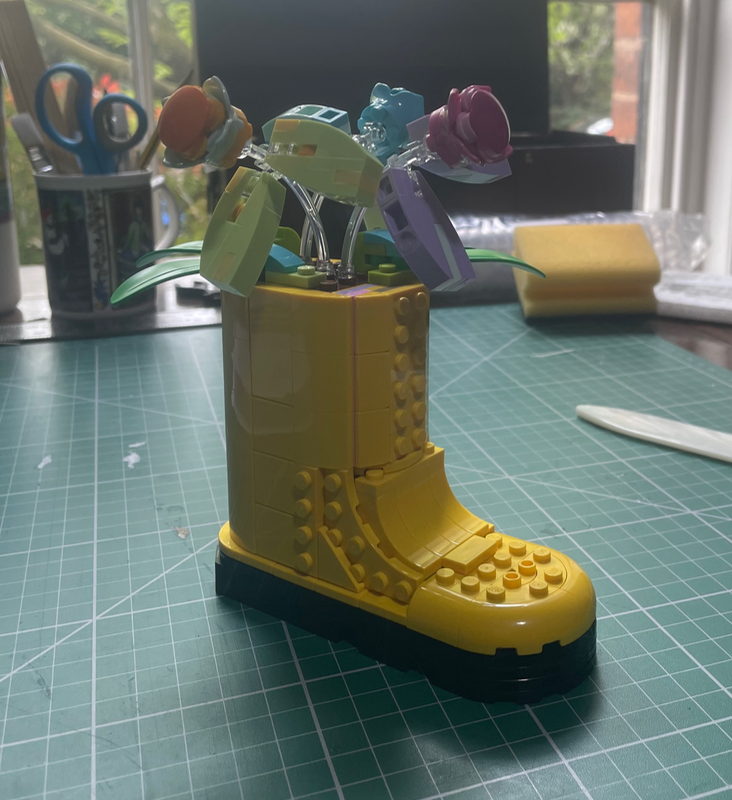 A yellow lego boot with buds in it with green and purple leaves.