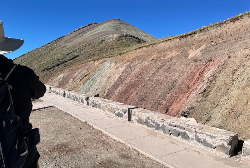A paved walkway, edged by rock and then a cut away bit of hillside revealin red, green and white stripes