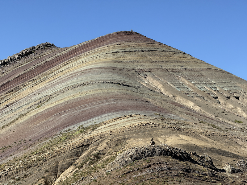 A hillside striped in mostly red, greens and yellows with a couple of bluey patches.