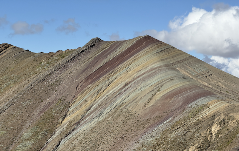 A hillside striped in mostly red, greens and yellows with a couple of bluey patches.