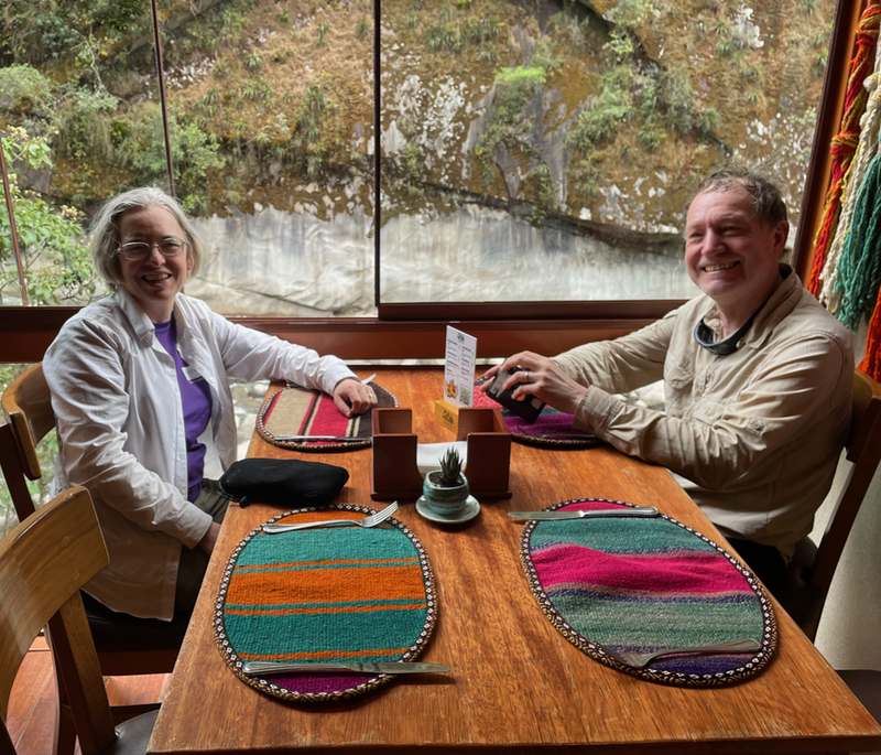B and I sitting by a Window looking out onto rocks and trees.  We're at a table with bright stripey place mats.