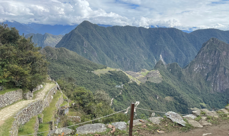Machu Picchu in the distance, a mountain behind, and Inca Trail and terraces to the left.