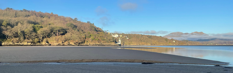 Wide shot of beach and a hill coming down to a white tower, buildings behind.