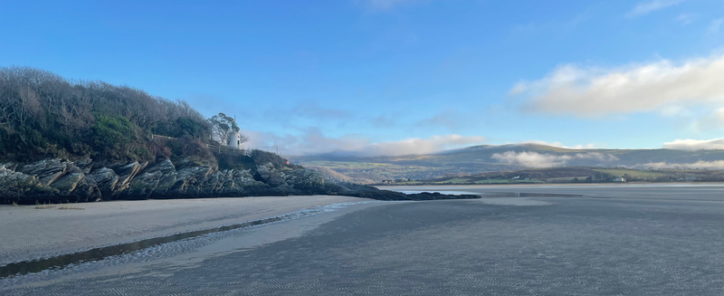 Wide shot of beach.  Clear blue sky.  A small white lighthouse is visible.