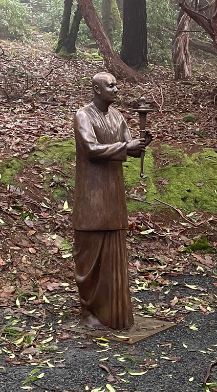 Bronze statue of a man in the dress of a Buddhist monk or similar, holding a ceremonial torch.