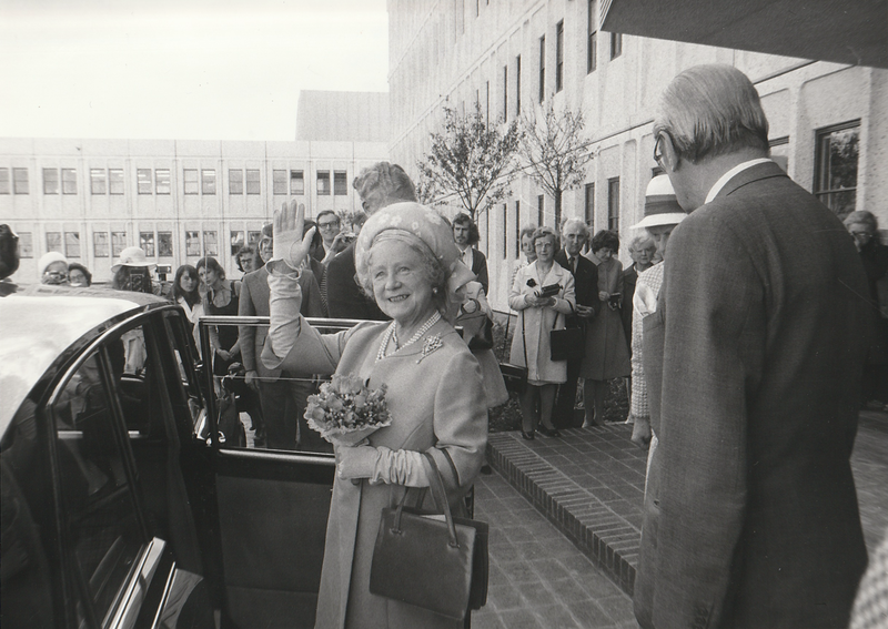 Black and White photo. The Queen Mum holding a bouquet, waving at the camera about to step into a car. A crowd is gathered behind. A cropped version of this shot appears in the second newspaper cutting.