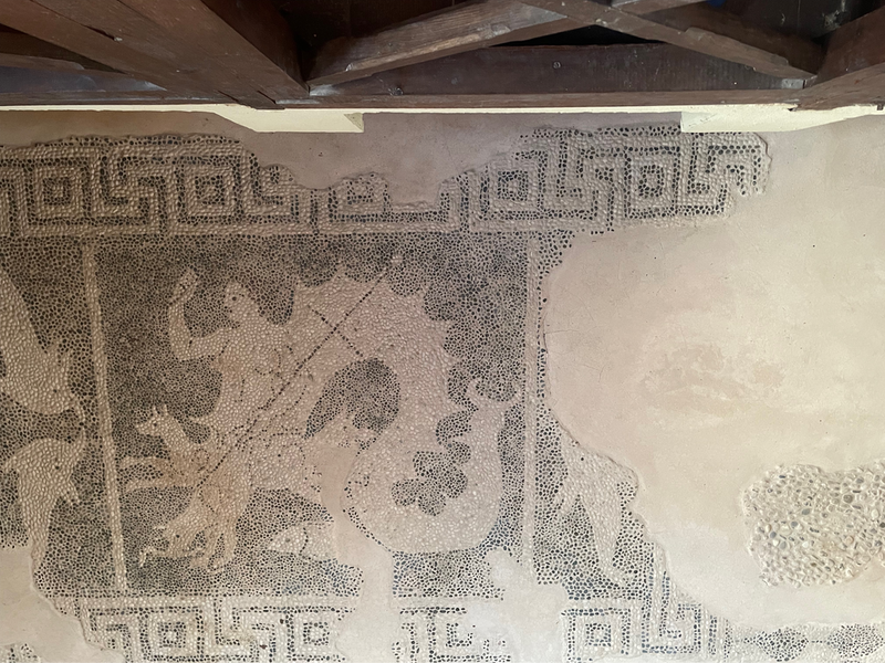 A black and white mosaic of a lady with a reptilian fishy tail, what looks like dogs instead of legs, holding some kind of spear