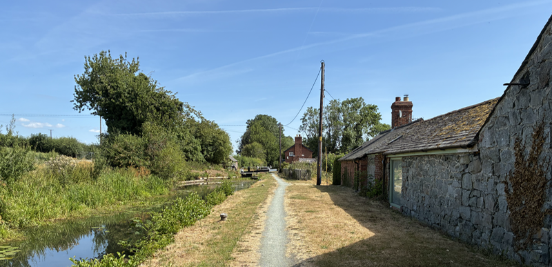A canalside with low buildings on the right and a lock in the distance.
