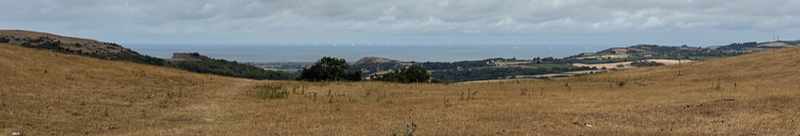 A view from a hill to the sea. If you look really carefully you can see a large wind farm.
