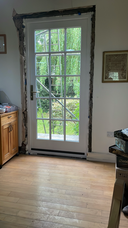 A glass door looking out onto a garden where scaffolding is visible. Plaster around the door is missing.