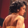 Belinda, head and shoulders from behind looking sideways in her yellow dress and 1950s hairstyle.