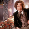 The Eighth Doctor seated in front of the Tardis console.