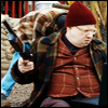 Nardole in a woolly hat.  Seated holding a gun and looking at something.