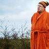 Nardole in an orange dressing gown with a bobble hat.