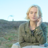 Ruby windswept on the phone.  The mysterious woman is just visible under a tree behind her.