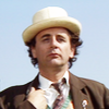 The Seventh Doctor.  Brown coat, head and shoulders, silhouetted against the sky.
