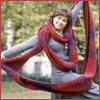 Publicity shot of Janet Fielding in a grey suit wrapped in Tom Baker's scarf which she is holding up arms outspread.