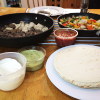 Table laid with flour tortillas, fried meat and peppers, soured cream and salsa