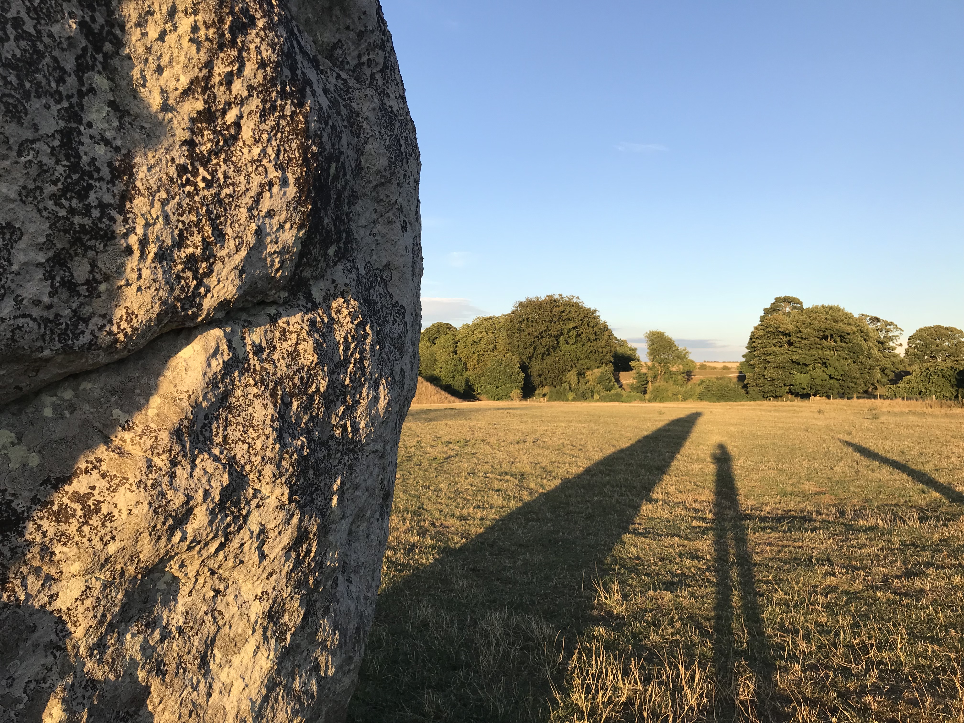 Edge of a stone casting a long shadow on the grass, as is the photographer.