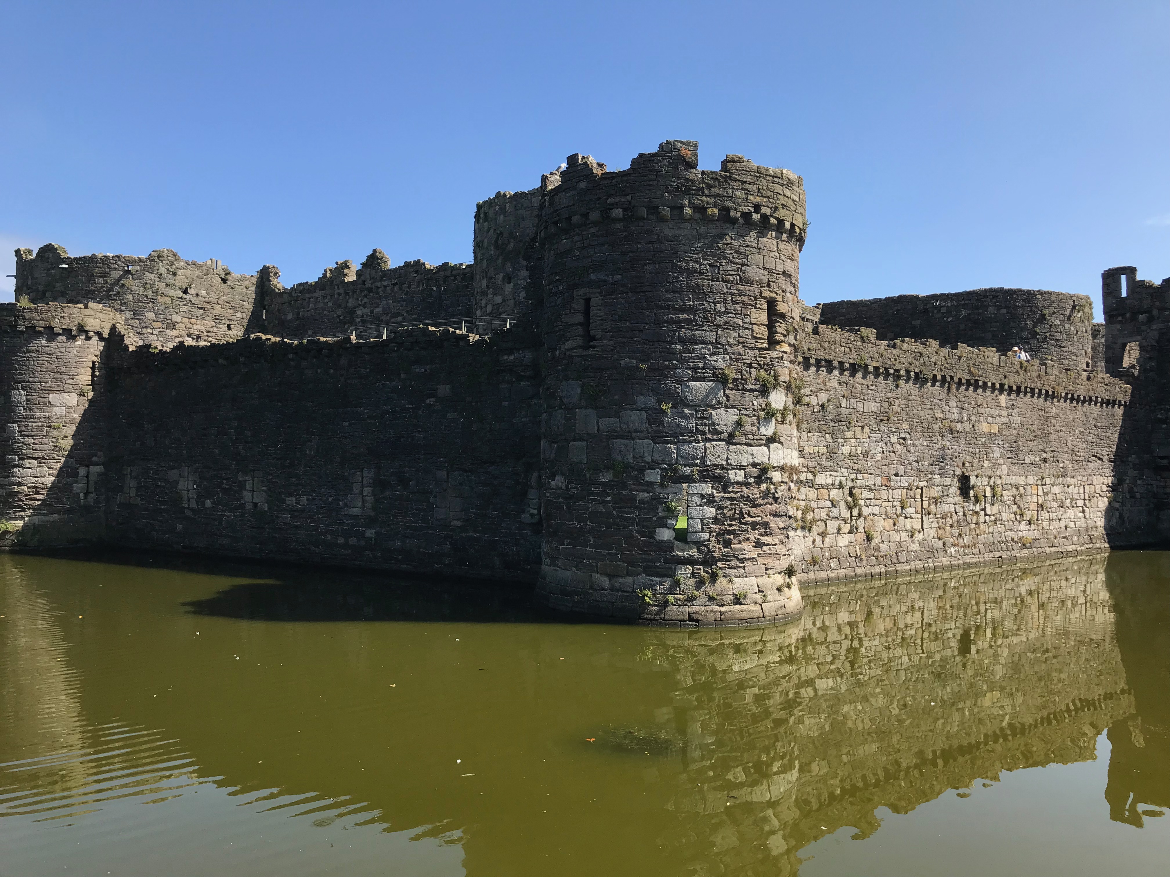 A round castle turret with walls going from it in both directions rising out of the water of a moat.