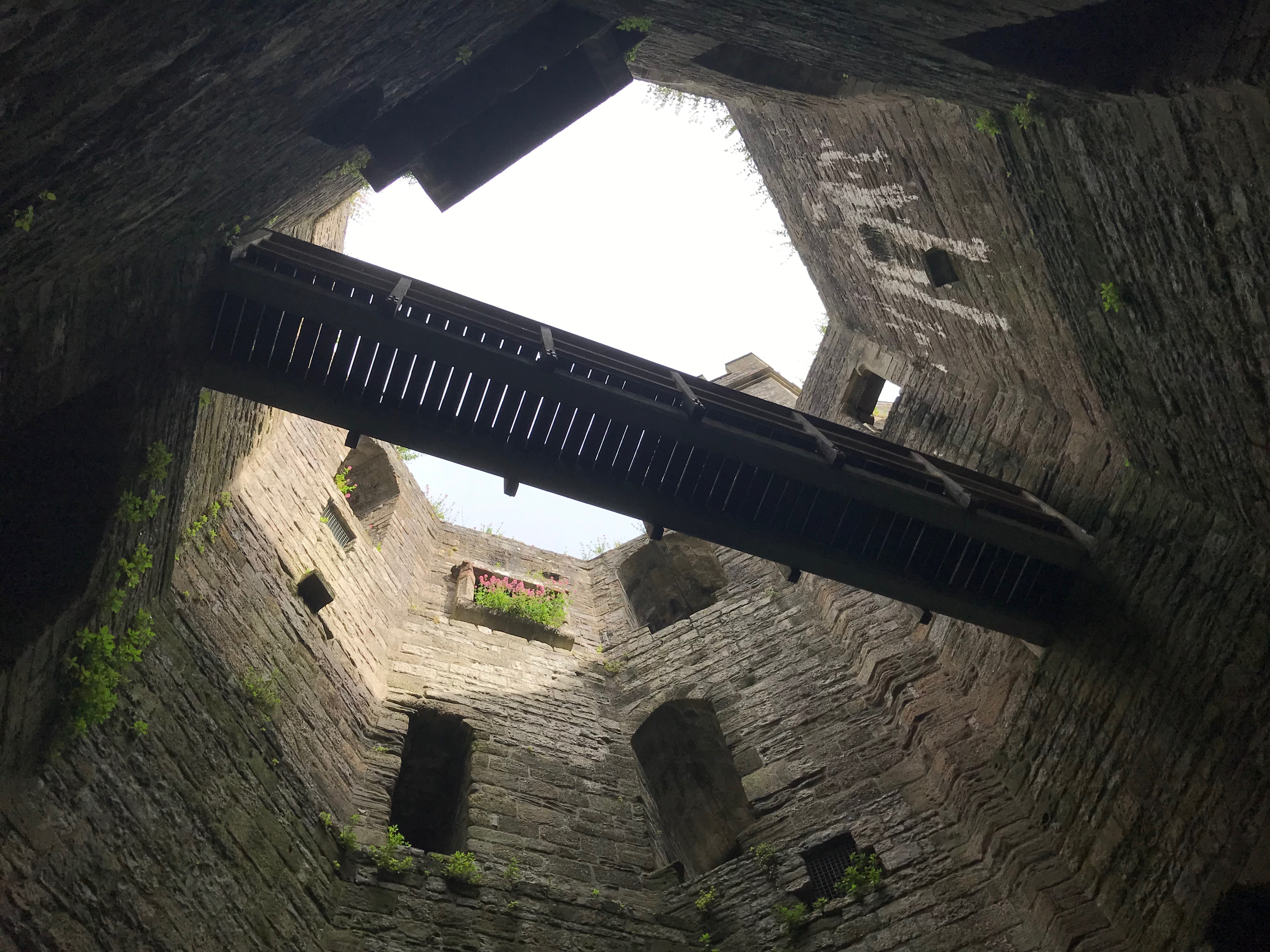 View upwards from inside an octagonal tower with no roof.  A wooden walkway spans the gap one floor up.