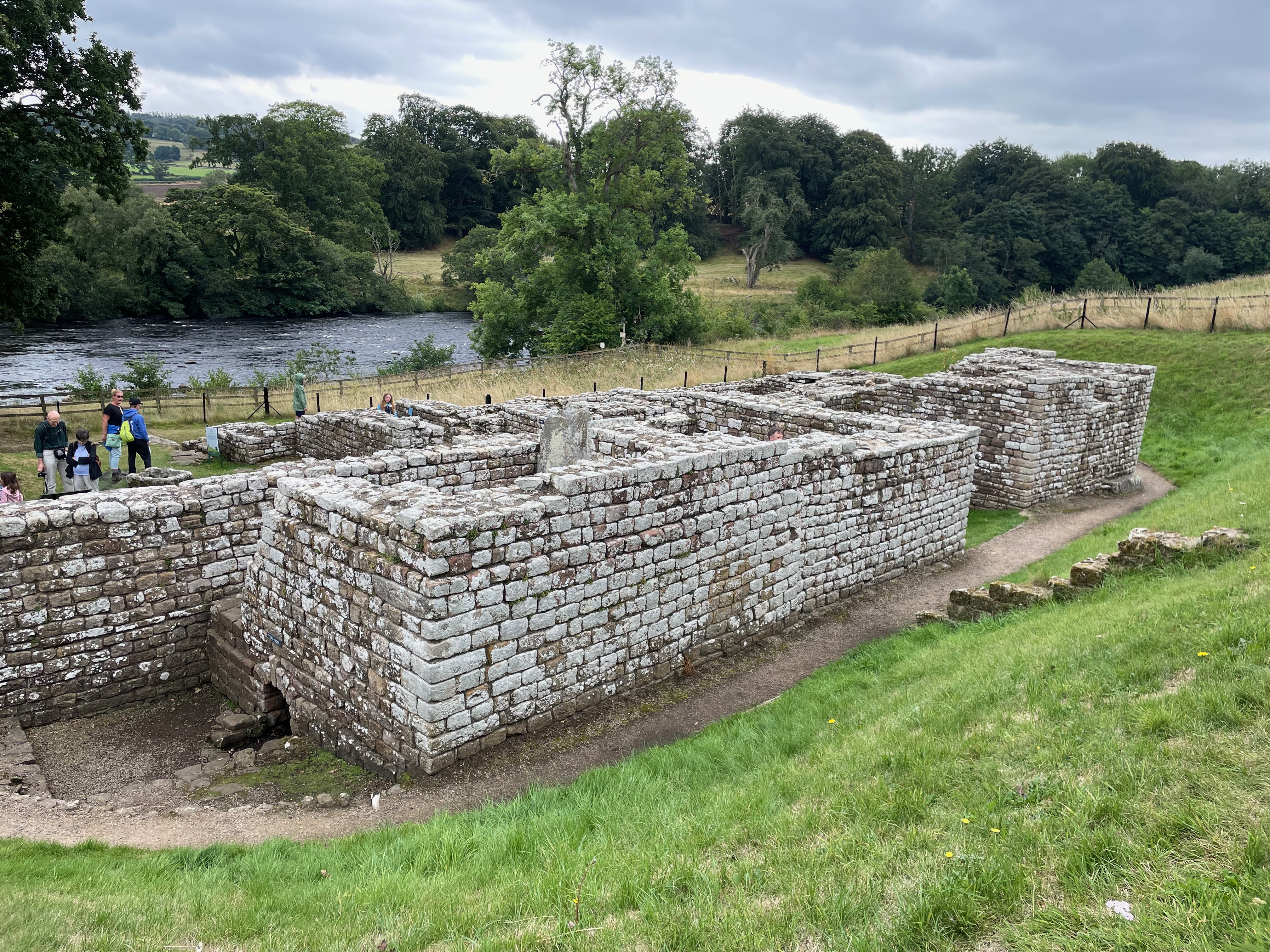 Ruins of squarish rooms with high walls on the banks of a river.