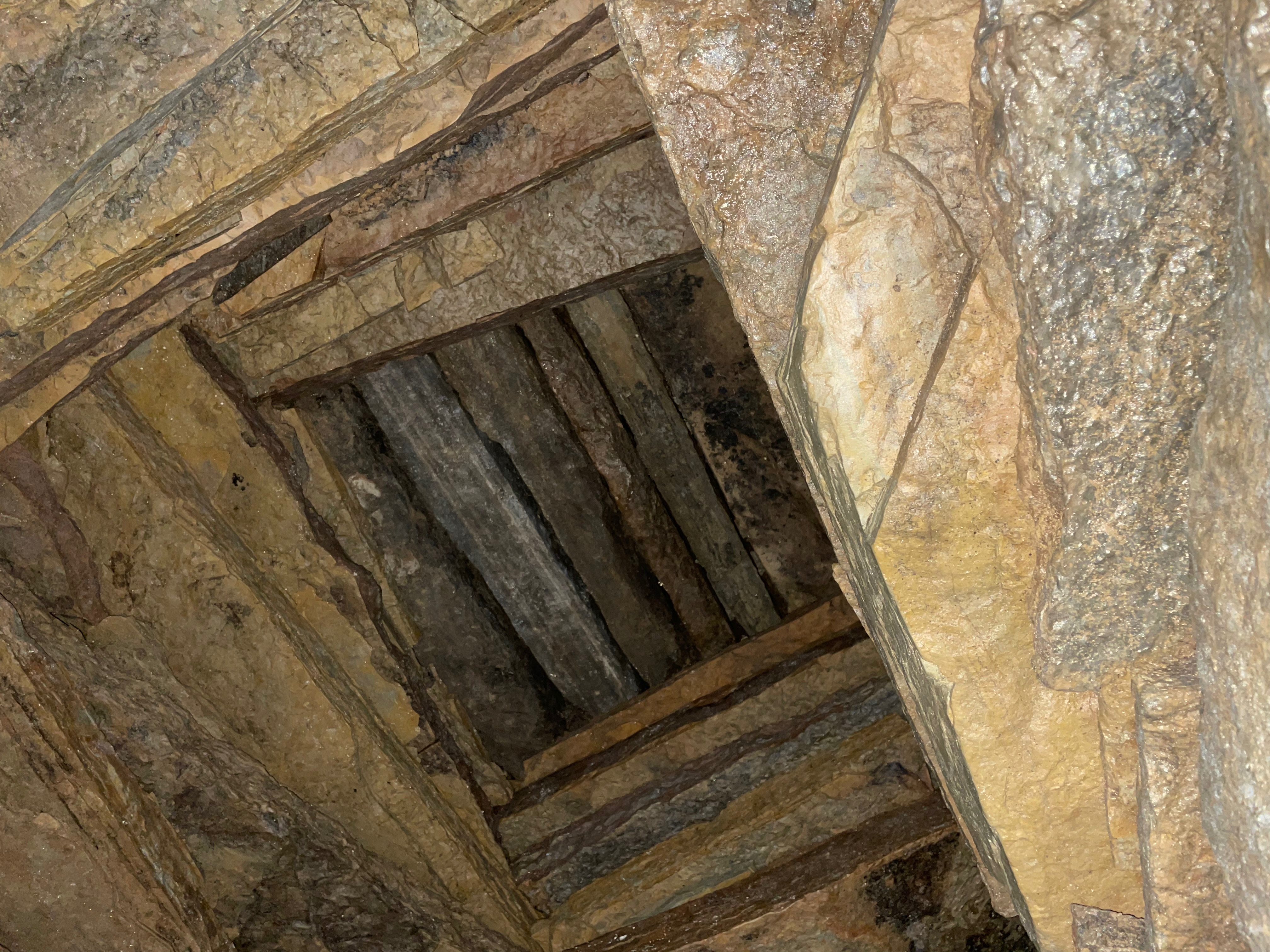 A view from the inside of stepped flat stones in a square shape leading upwards.  The square hole at the top is covered by a row of stone slats.