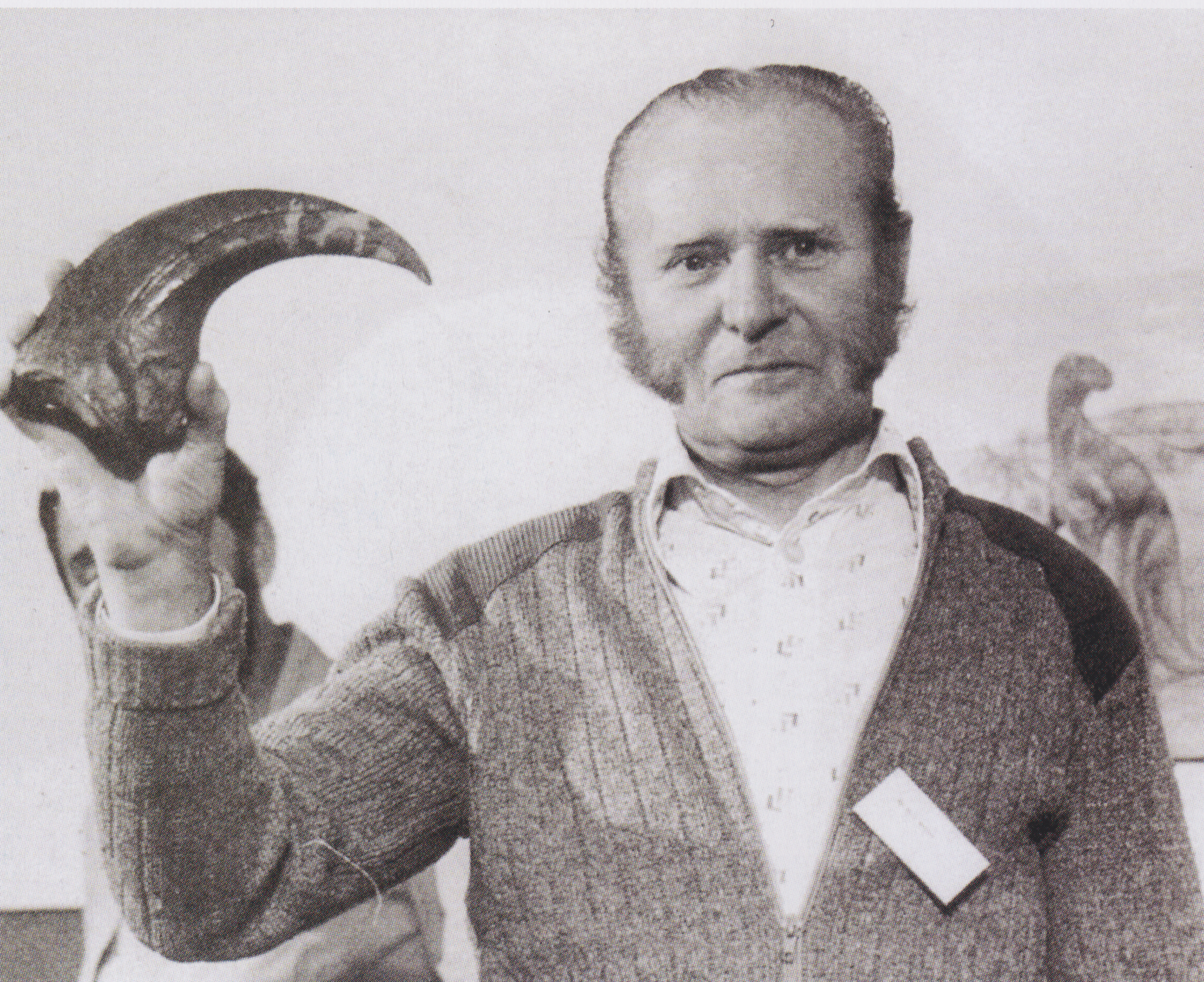 A black and white photo of a gentleman with moderately impressive sideburns and what, I am sure, was a very impressive cardigan holding a large fossilised dinosaur claw.