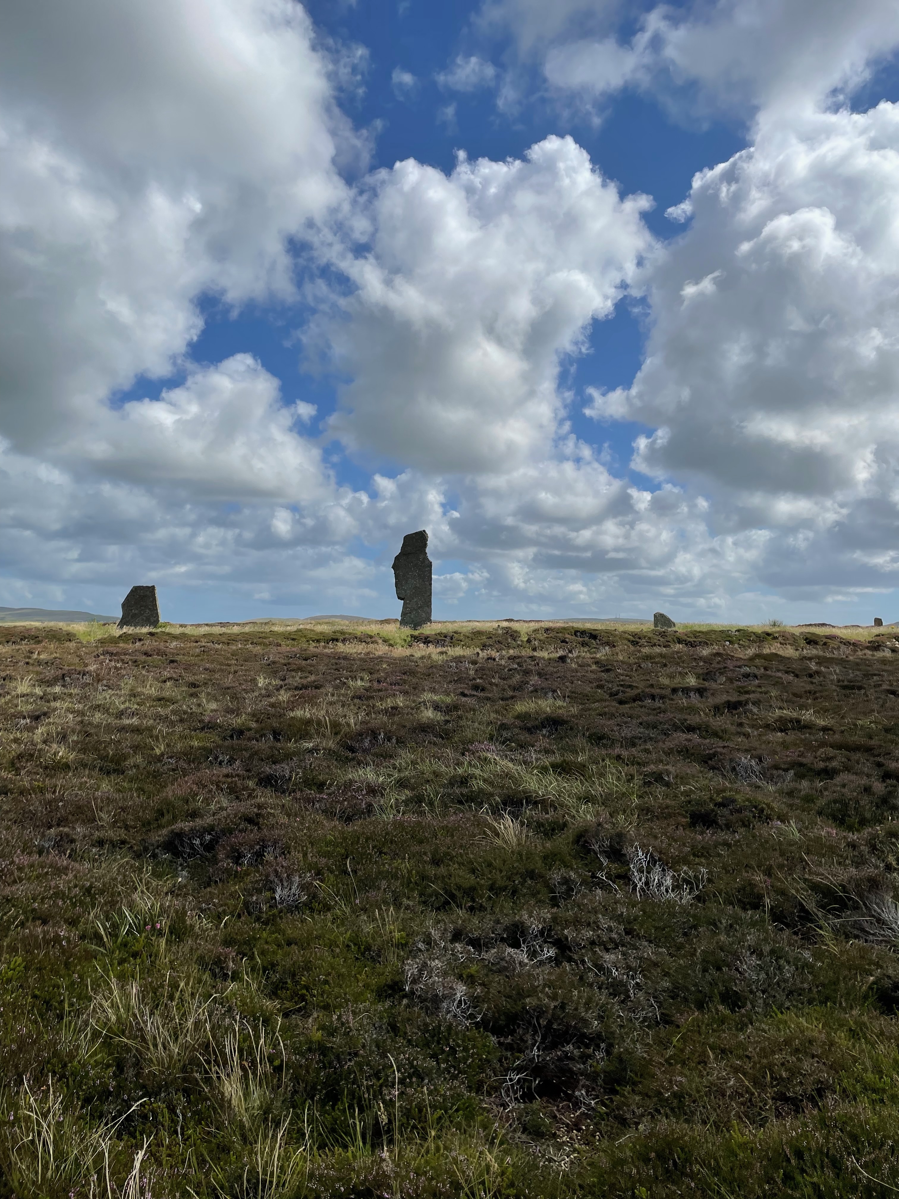 A standing stone silhouetted against a dramatic blue sky with clouds.