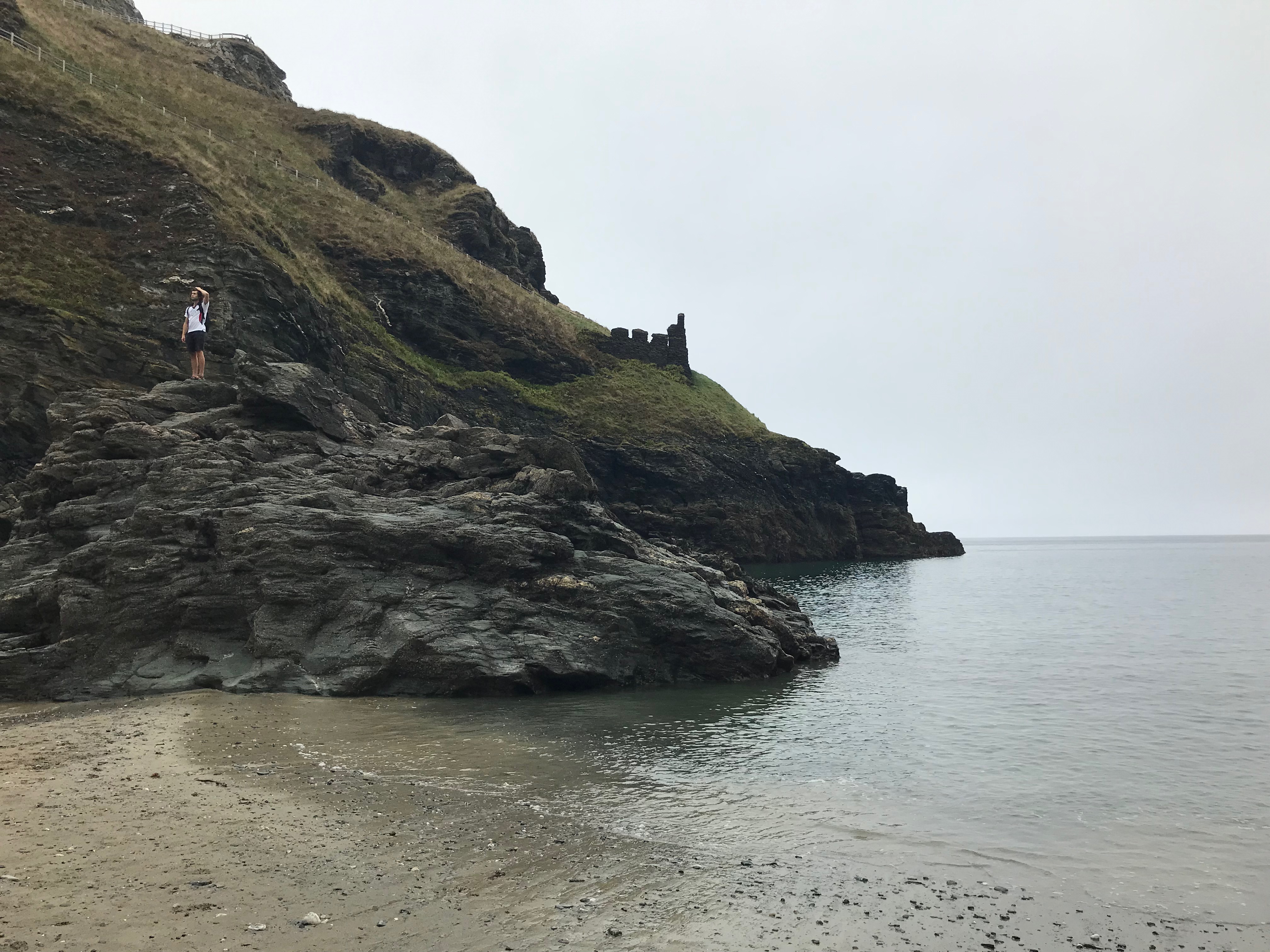 Grassy slope leading to rocks and then the sea and a beach.  A small ruin with battlements is visible halfway down.