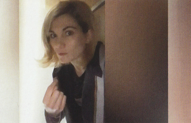 Jodie Whitaker as the Thirteenth Doctor looking around the door of a cupboard and pointing at herself.