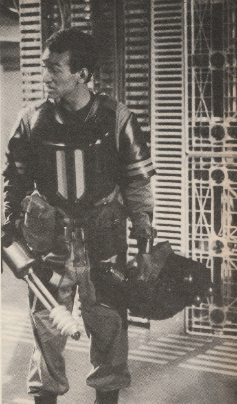 Black and White Photo of Mercer from Resurrection of the Daleks, disguised as a Dalek trooper holding helmet and gun.