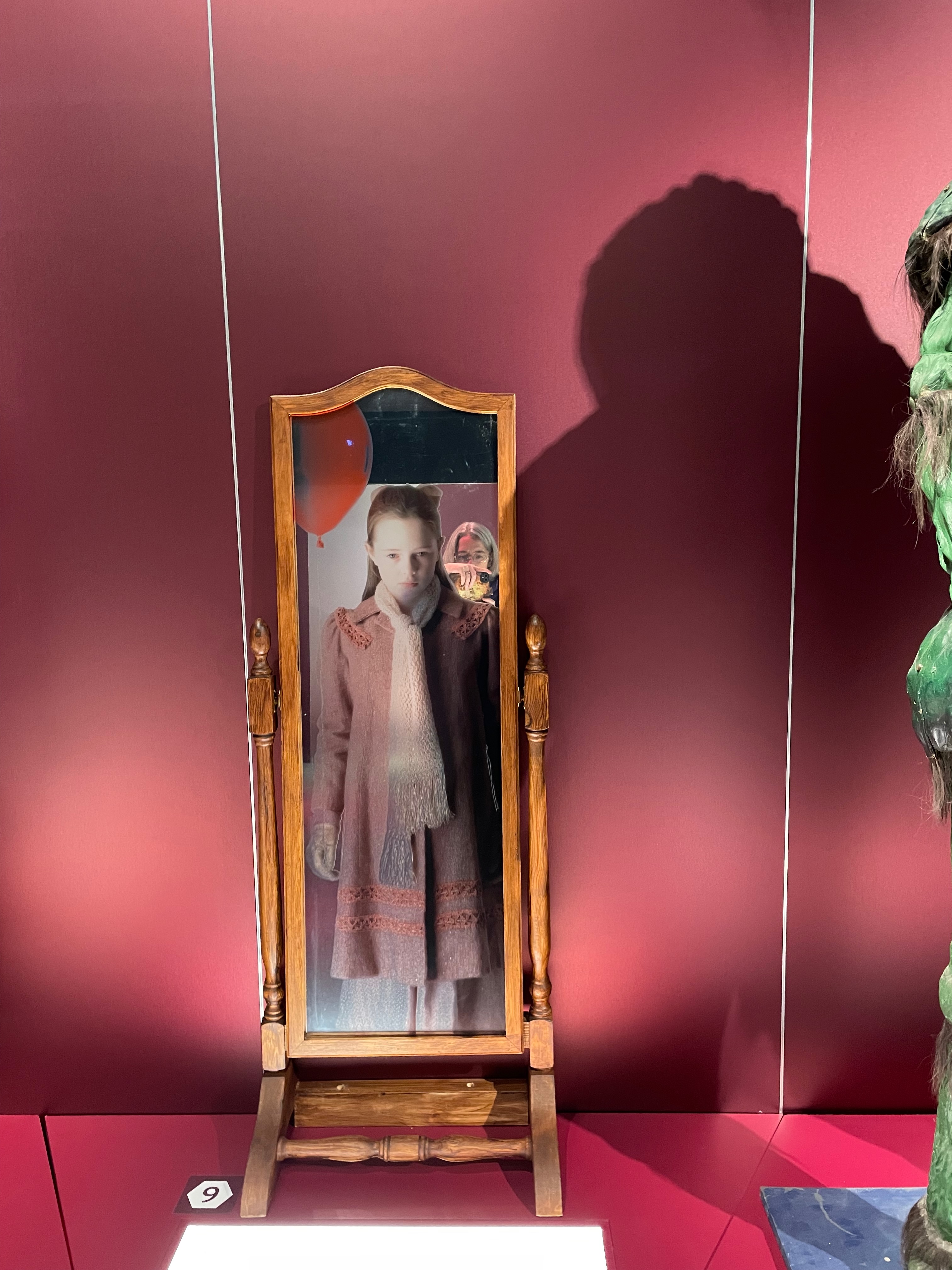 A mirror containing a girl with a balloon. The photographer is just visible behind.